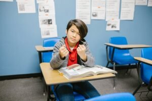 A young student with a determined expression sitting in a classroom holding a pencil.
