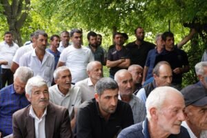 A diverse group of men gathered outdoors under trees, engaged in an event.