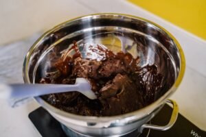 Delicious chocolate melting in a stainless steel bowl over a stove with a spatula.
