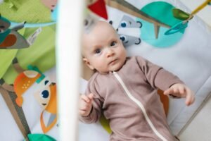 Cute baby in a onesie enjoying playtime on a colorful mat indoors, captivating with innocence and creativity.
