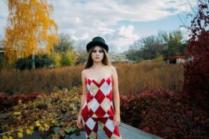 Woman in argyle dress and top hat standing in a vibrant autumn landscape.