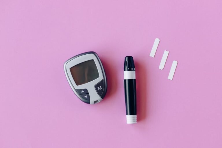 Flat lay of diabetes testing kit with glucometer and lancet on pink surface.