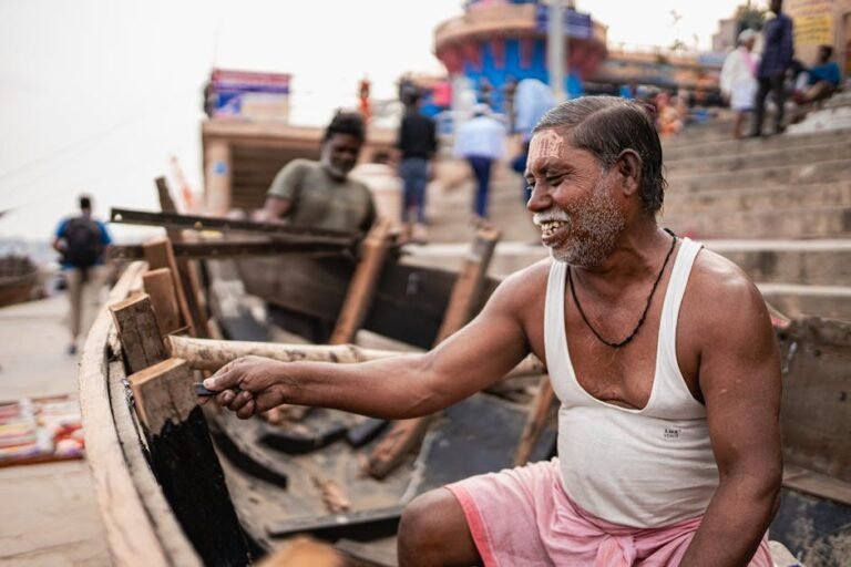 An elderly man fixing a wooden boat at the historic ghats of Varanasi, India.