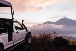 A pickup truck parked on a cliffside with scenic mountain views at sunrise.