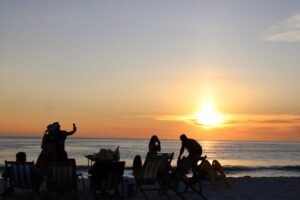 Silhouette of people enjoying a tranquil sunset on the beach.