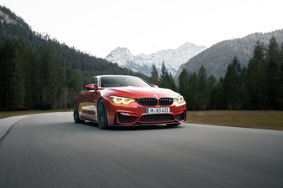 A stunning red BMW car speeds along a forest road with majestic mountains in the background.